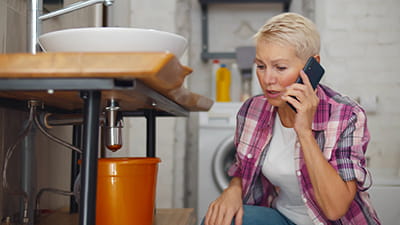 A person on the phone to her plumber next to a leaking pipe