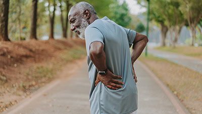 A mature man holding his back while out for exercise