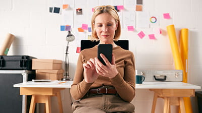 Mature businesswoman with mobile phone working at desk in start up creative business