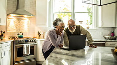 Senior couple using laptop in kitchen of suburban home