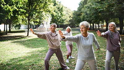 Group of senior friends doing tai chi exercise outdoors in park.