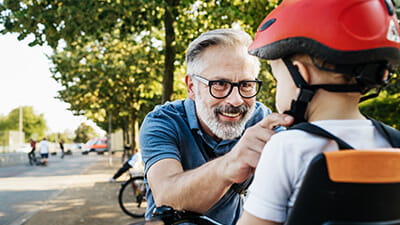 A mature man helping his grandson put his bicycle helmet on