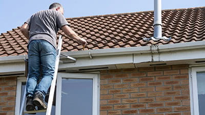 Senior man cleaning gutters on a suburban English house.