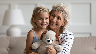 A grandmother and granddaughter in a happy embrace while wearing tiaras