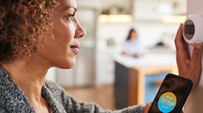 A woman adjusting her thermostat and looking at the app on her smartphone