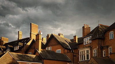Pitched roofs and chimneys of traditional brick houses in England underneath dark storm clouds