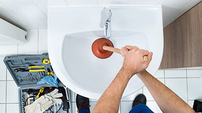 Close up aerial view of a plumber using a plunger on a sink