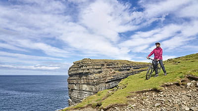 A mature cyclist, taking in the view from the edge of a cliff on a sunny day.