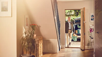 A mature man walking in to his house with a bag of fancy shopping.