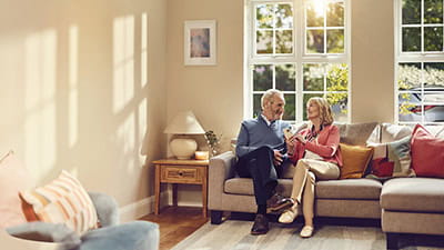 A happy mature couple enjoying what they see on their phones while sat together in their living room