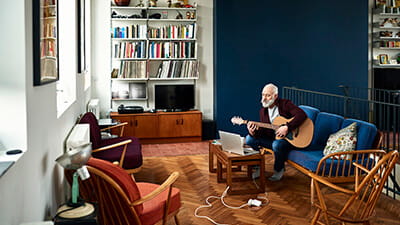 Senior man practising guitar at home in retro living room