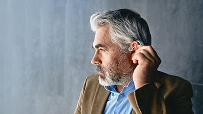 Grey-haired mature man with hearing impairment using hearing aid.