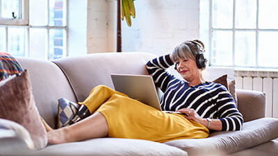 Senior woman wearing headphones watching movie on laptop