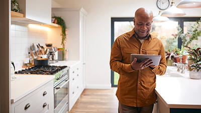 A man stood in his kitchen looking at his tablet computer