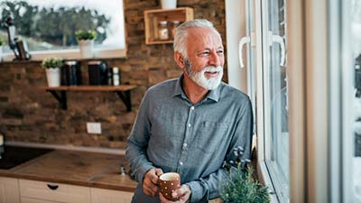 A man looking out of his kitchen window enjoying a coffee