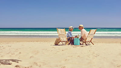 A happy mature couple relaxing by the sea on deck chairs with a bottle of champagne.