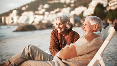 Happy senior couple relaxing on deck chairs at beach