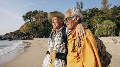Happy senior couple standing with arms around and looking at sea on beach