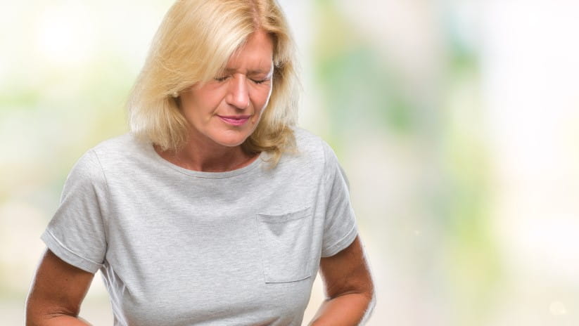 A woman in a grey t-shirt clutching her stomach