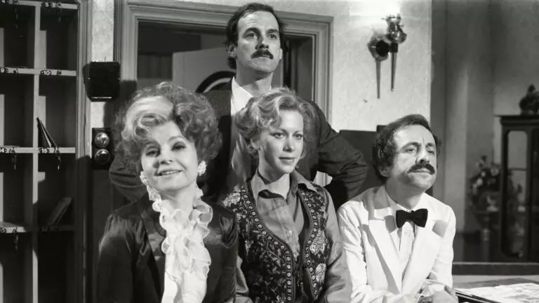 Black and white photo of the cast from Fawlty Towers on set at the hotel reception