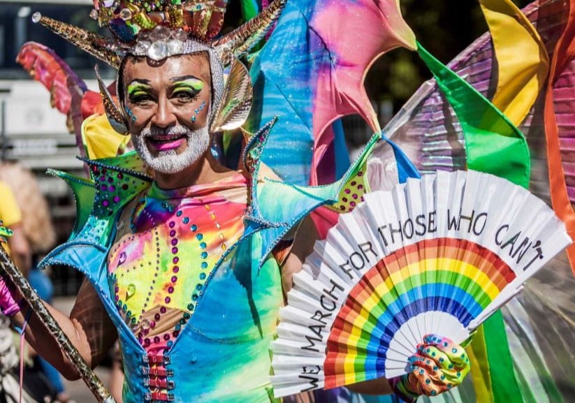 Person in colourful dress and clothes waving a Pride fan