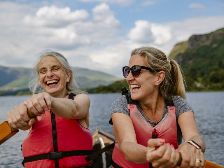 Two older women having a joyful time rowing a boat on a lake | Getty