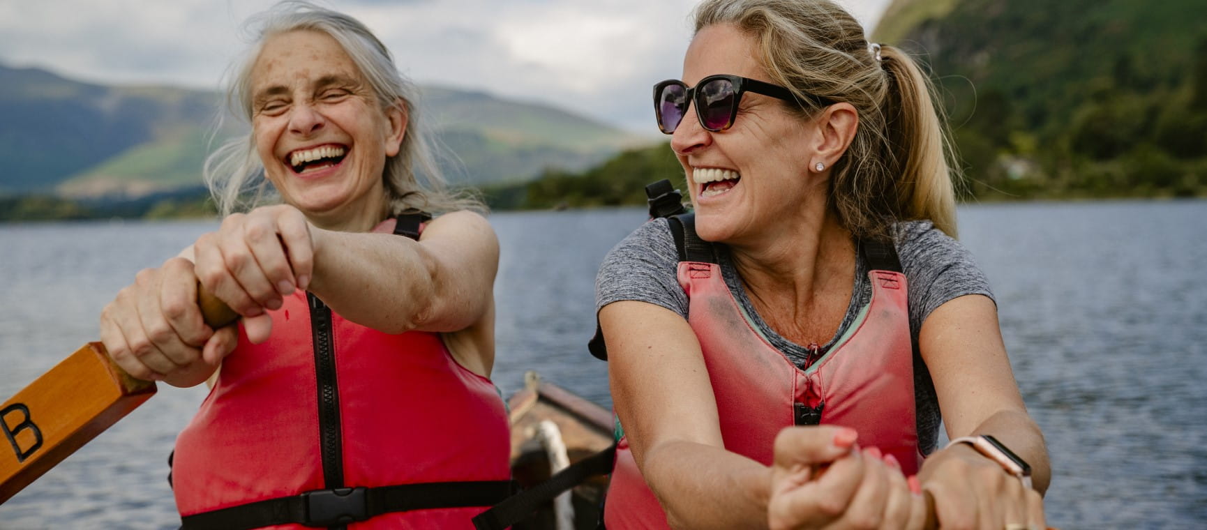 Two older women having a joyful time rowing a boat on a lake | Getty