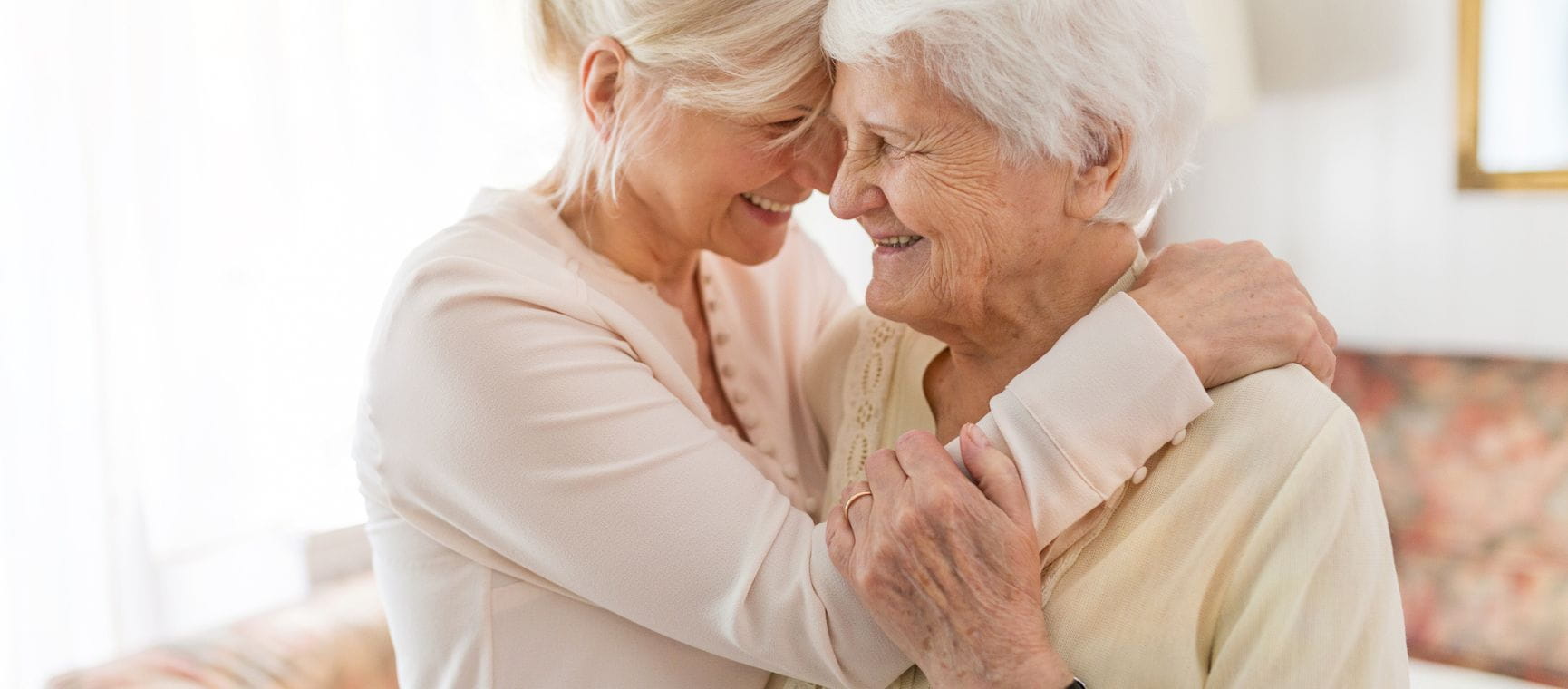 an older woman giving her mum a hug, with both of them smiling