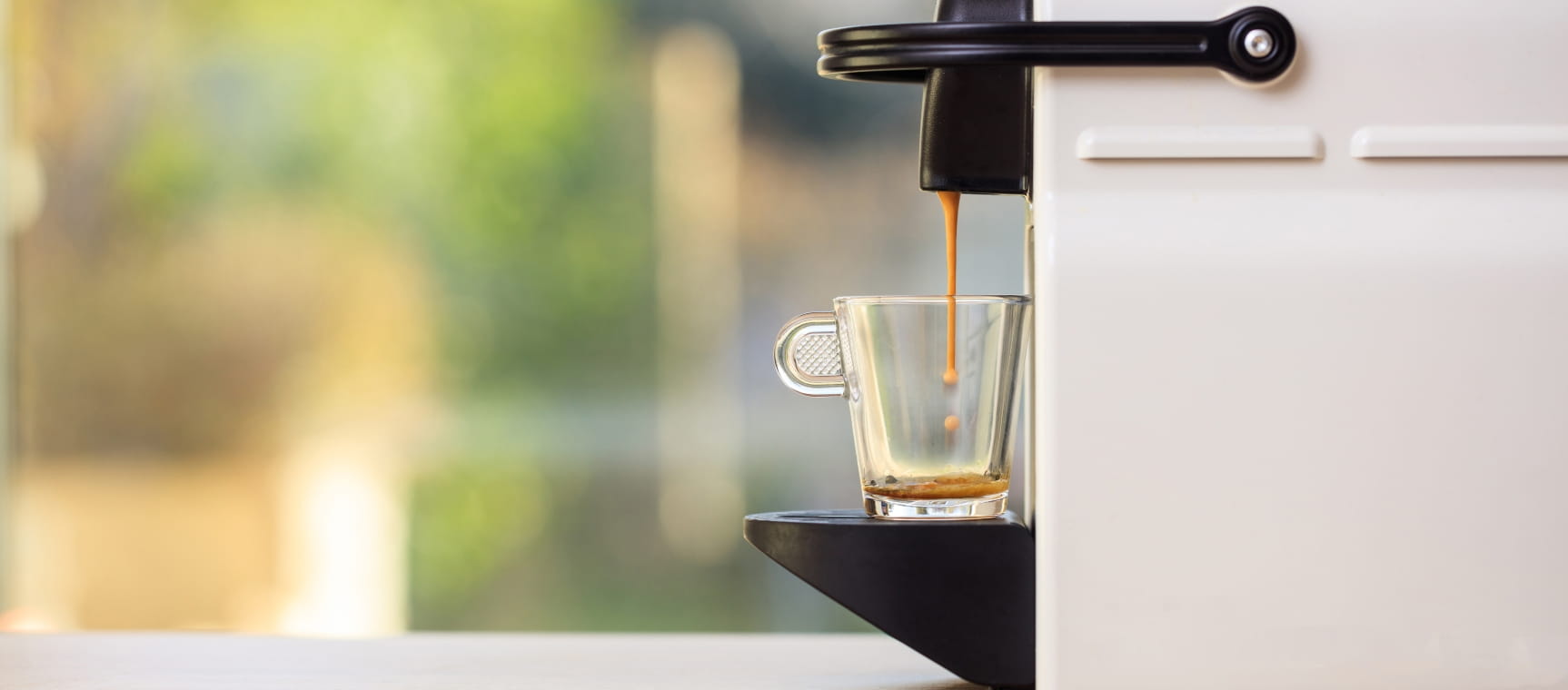 Close-up of the side of a coffee pod machine dispensing an espresso shot into a small glass