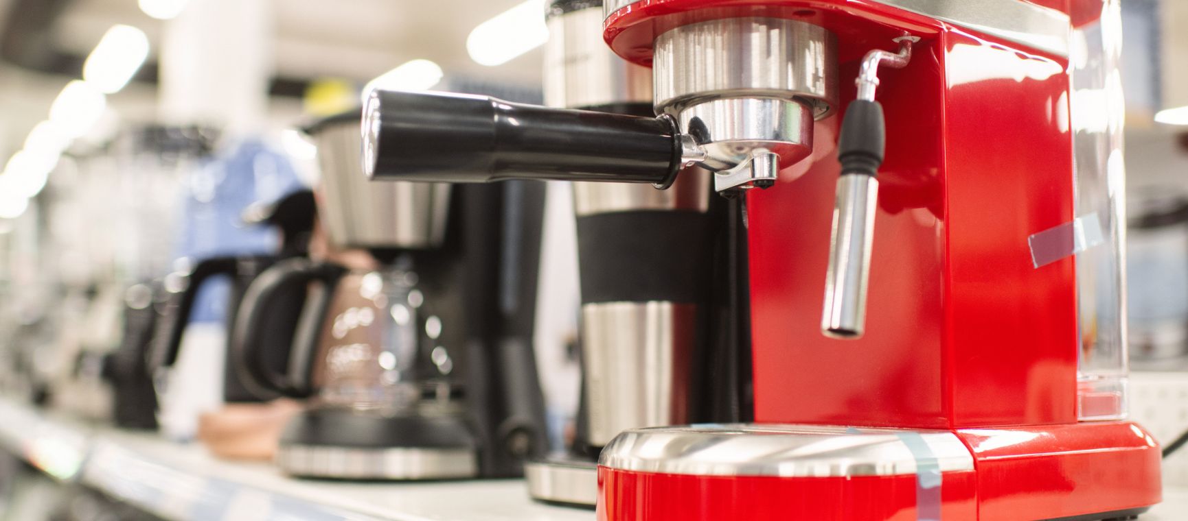 A row of different coffee machines in a shop with a bright red espresso maker in the foreground