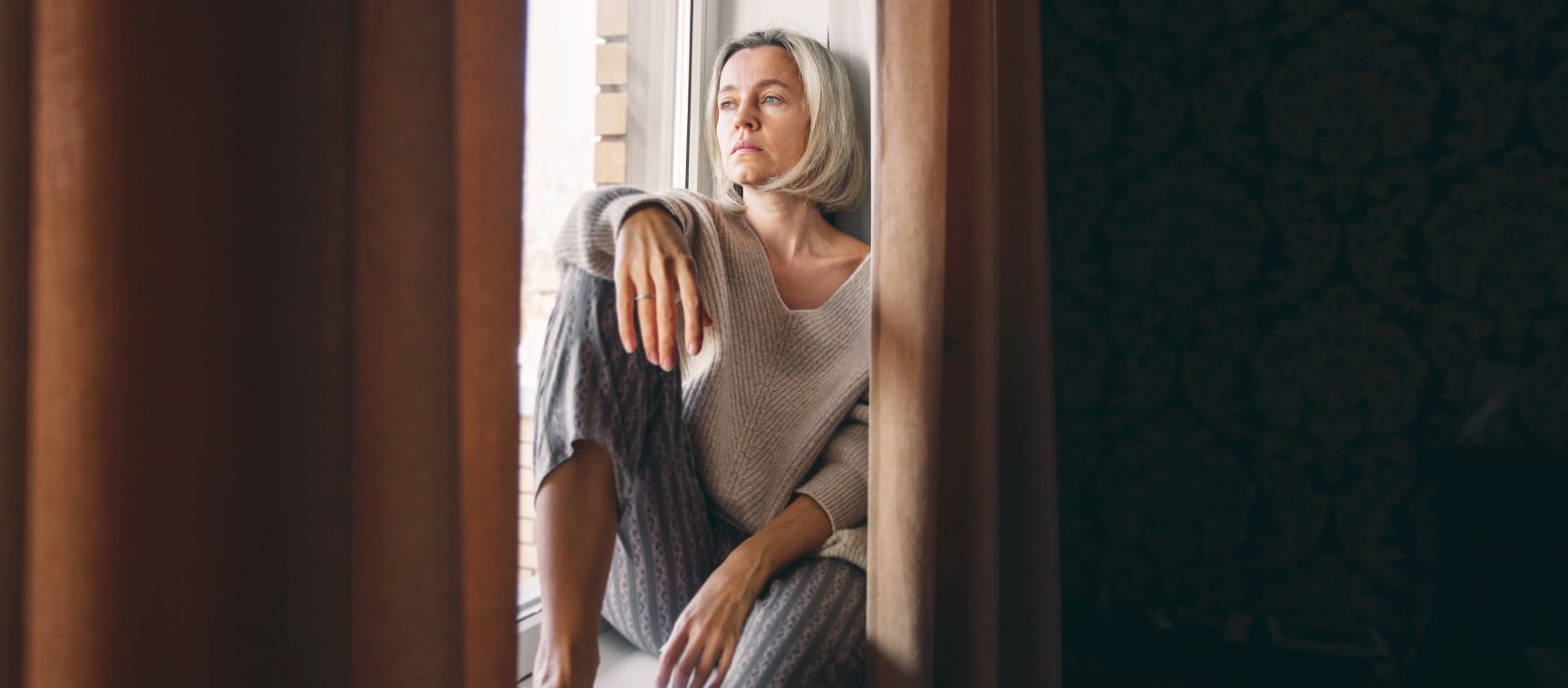A woman sits thoughtfully looking out of a window | Getty/TatyanaGl