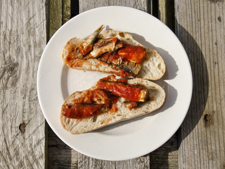 Two slices of bread with sardines in tomato sauce on a white plate on a wooden table on a sunny day | franswillemblok