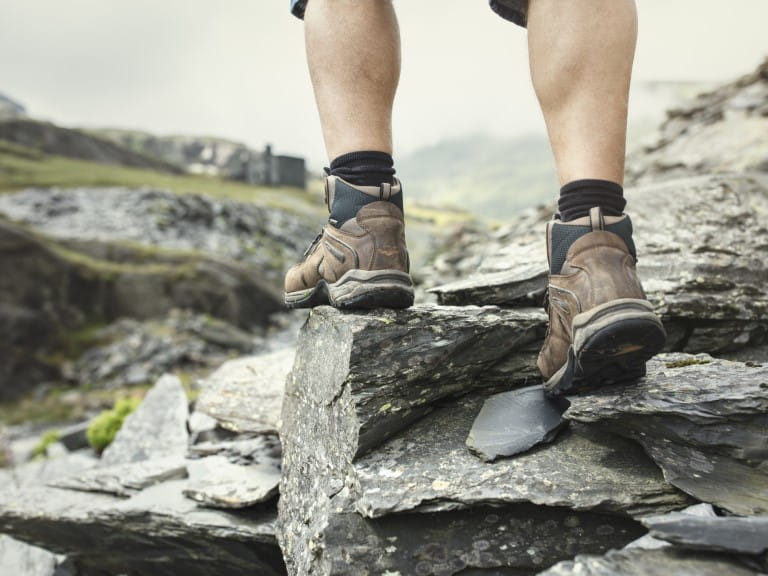 A man in walking boots heads away from the camera over rocky terrain