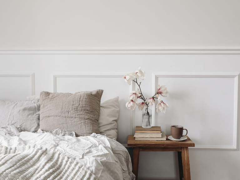 A neutral bedroom with a wooden side table and neutral bedding