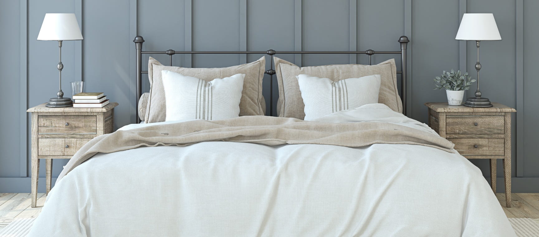 Bedroom with a panelled grey wall and neutral furnishings, with two wooden bedside tables with stylish lamps