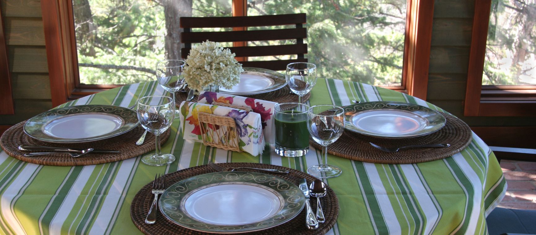 A dining table in a conservatory with a green striped tablecloth all set for lunch