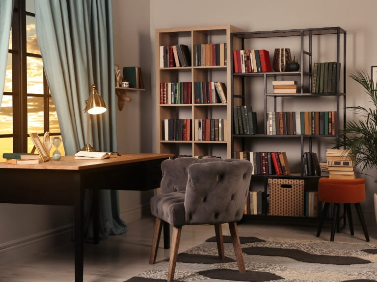 A comfortable home office with large desk, bookshelves and a comfortable chair, lit with ambient desk lighting