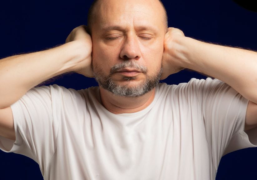 A man with a beard with his hands over his ears