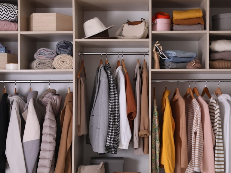 The inside of a large wardrobe with hanging clothes, folded garments, hats and bags inside