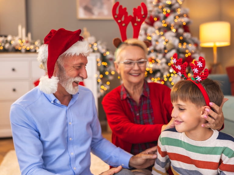 A senior couple with their grandchild at Christmas, all wearing Christmas headbands and hats