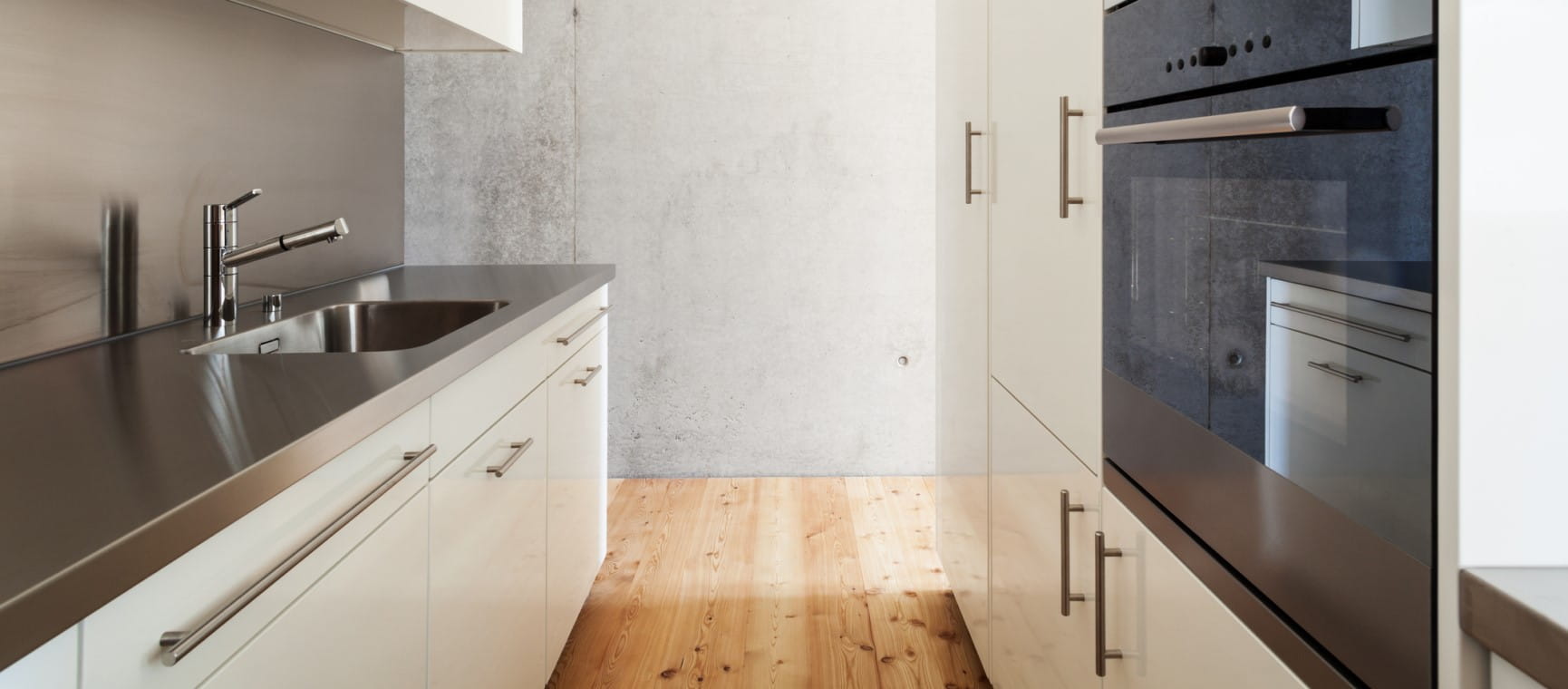 A narrow galley kitchen with white furnishings with a concrete background wall