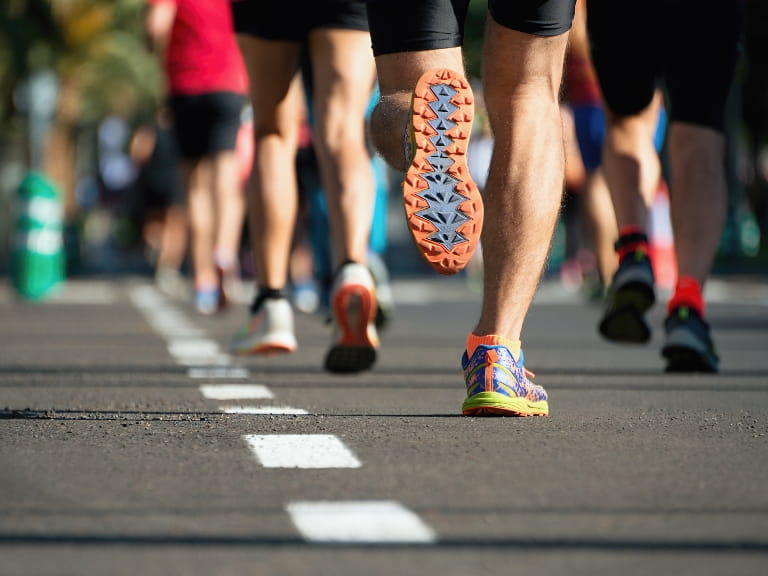 Legs and feet of runners during a race; the bottom of a running shoe kicked up as a runner embarks on a race
