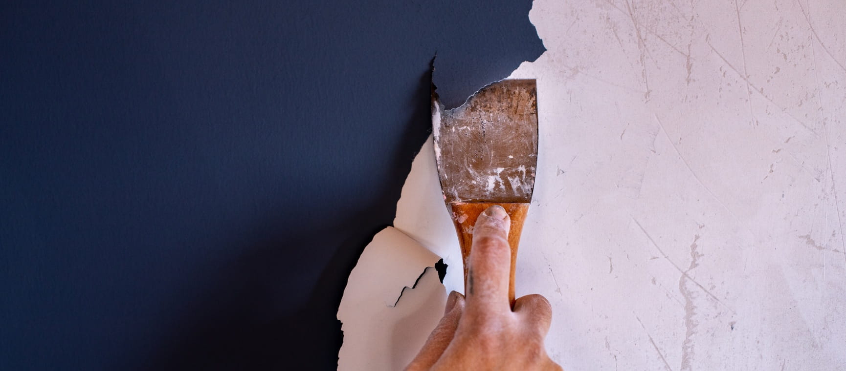 Close-up of dark blue paint being scraped off a wall using a paint scraper