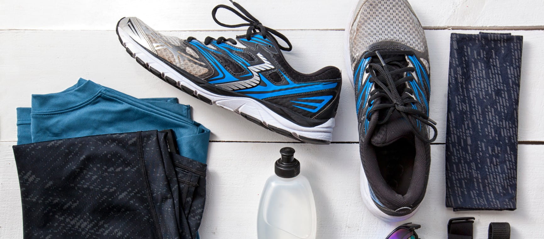 Running gear essentials including a pair of black and blue trainers, sports clothes, water bottle and neck warmer
