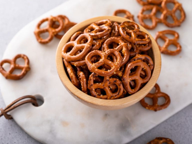 Mini pretzels in a wooden bowl, salty healthy snack | Getty/VeselovaElena