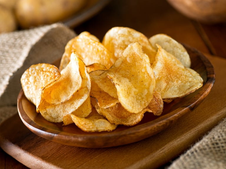 Delicious home made potato chips with sea salt and black pepper against a rustic background | Getty/Fudio