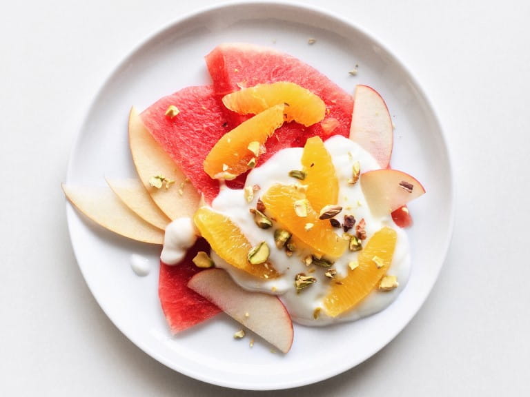Plate of fresh fruit salad with yogurt, watermelon, orange, apple, and pistachio on a white background | Getty/SEE D JAN