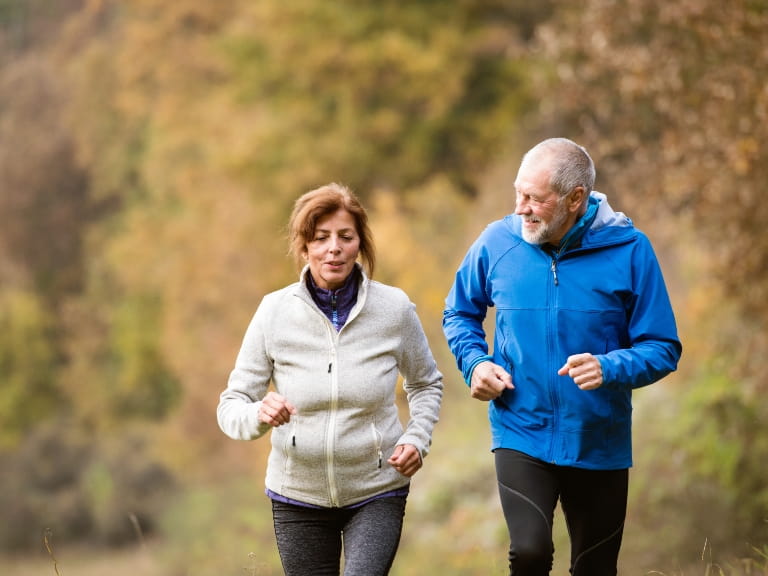 A mature couple smiling while enjoying a run outdoors in autumn