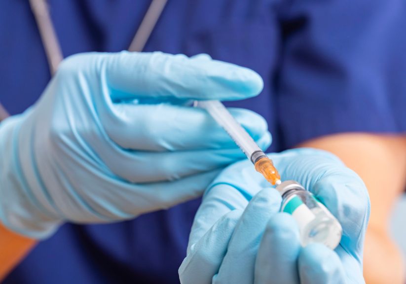 A doctor with gloved hands preparing a vaccine to be injected