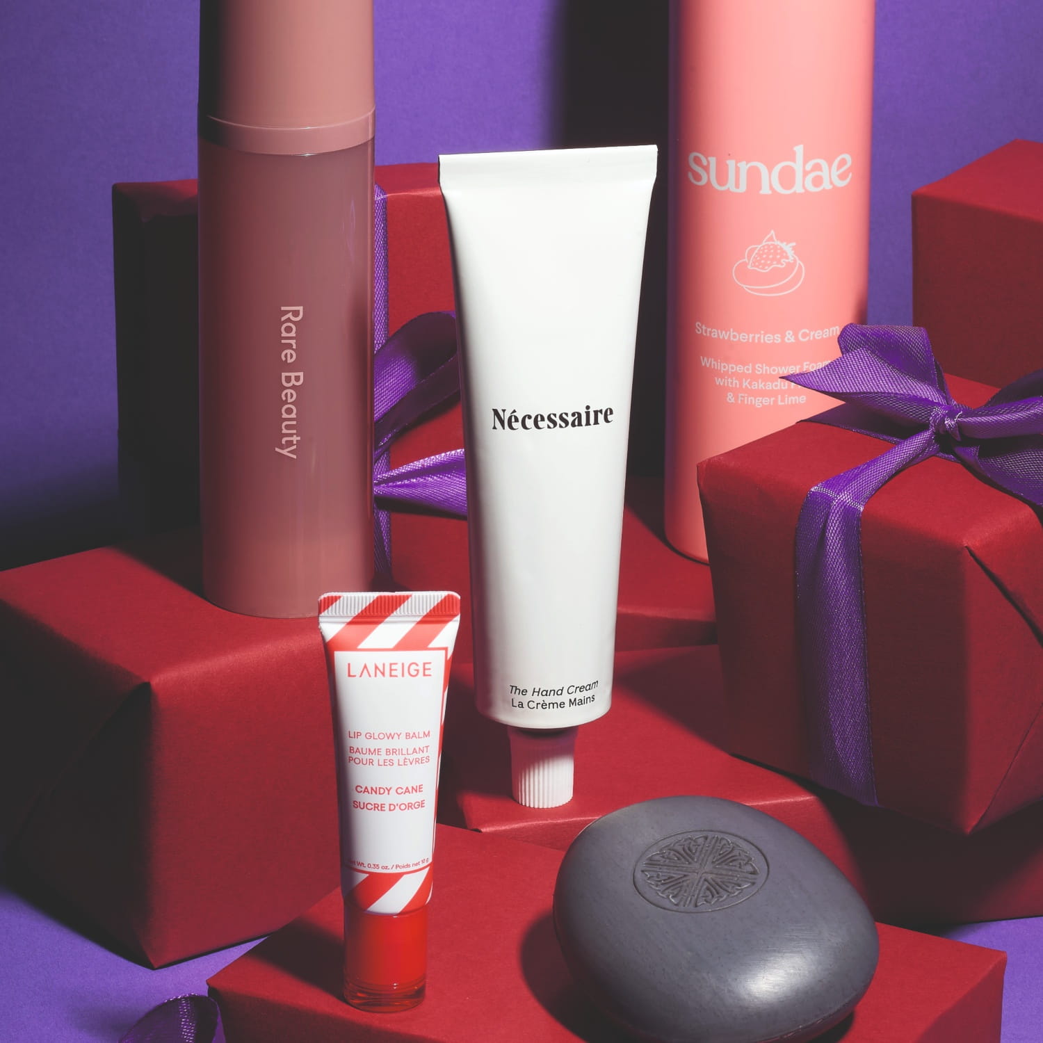 Beauty products that make great gifts displayed with red boxes, including body mist, hand cream, palette, lip gloss and shower foam.